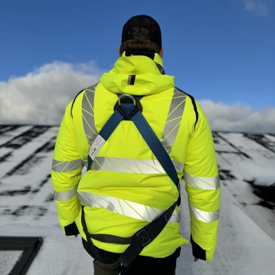 blå och svart fallskyddssele på man i varseljacka på tak gåendes uppåt