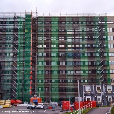 Grön och svart sommarväv ställningsväv i byggställning mot stort hus