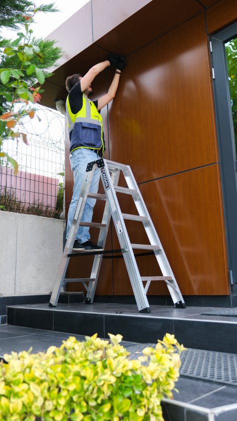 Person i varselkläder står och arbetar på en stege utomhus 